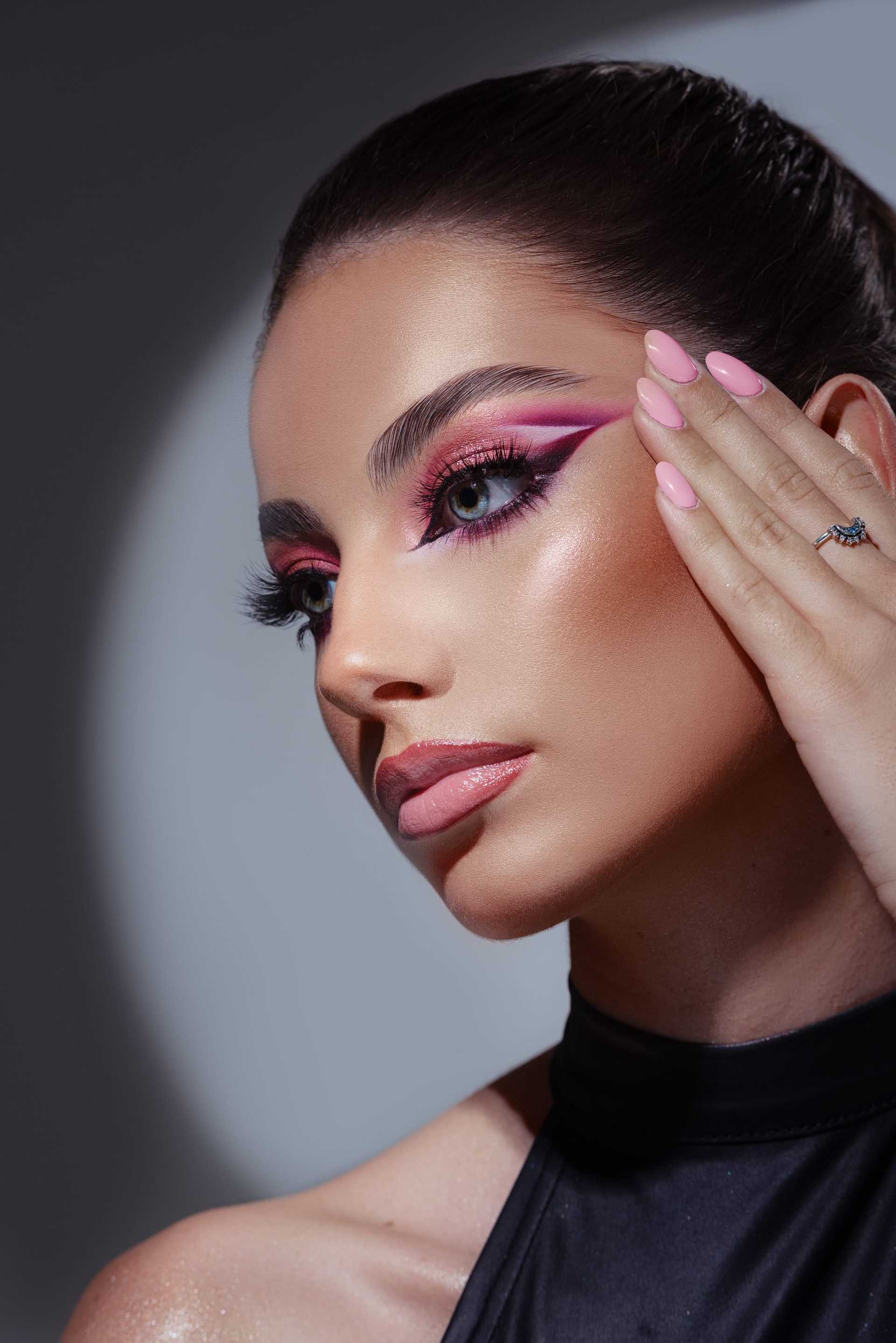 Woman with bold pink eye makeup and manicured nails against a soft-focus dark background.