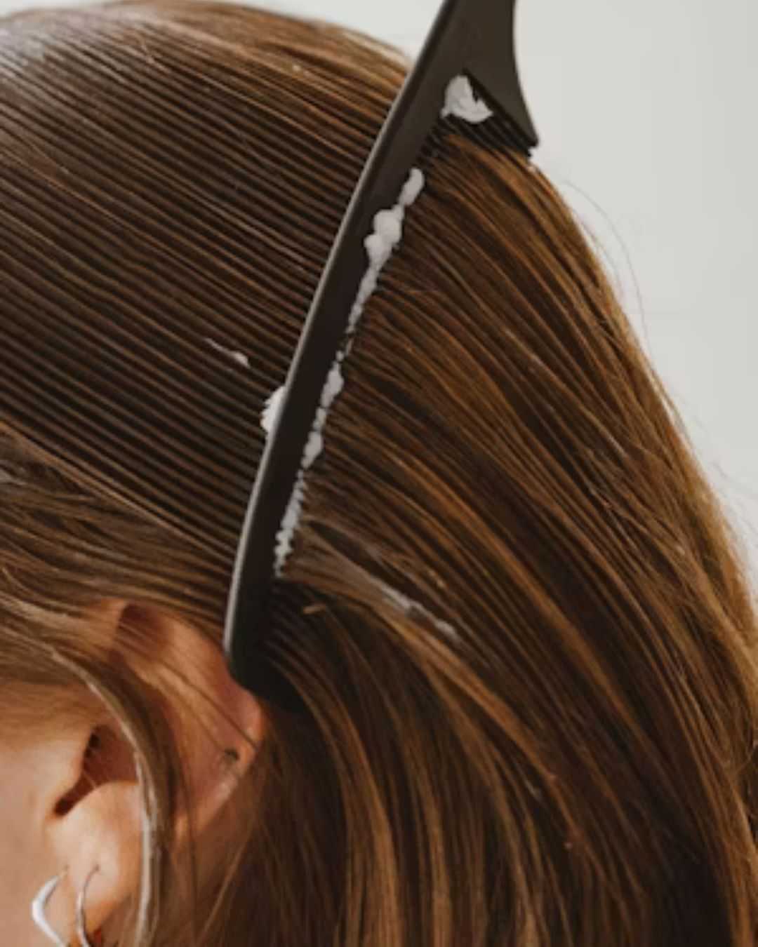 Comb spreading hair product through brown hair.