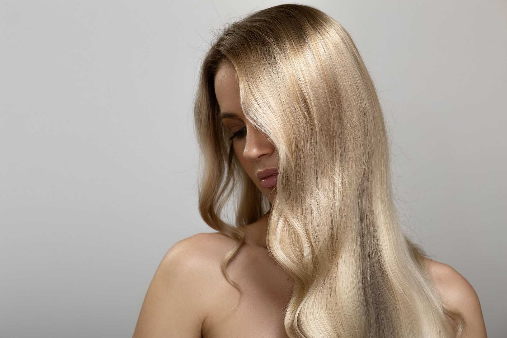 Woman with long, smooth blonde hair partially covering her face against a neutral background.